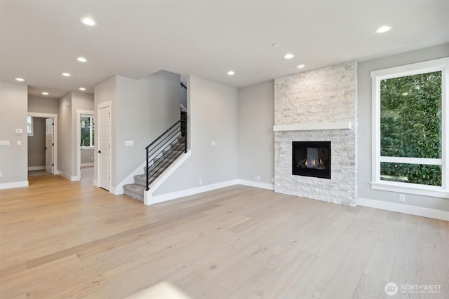 unfurnished living room with a healthy amount of sunlight, light wood-style floors, a stone fireplace, and recessed lighting