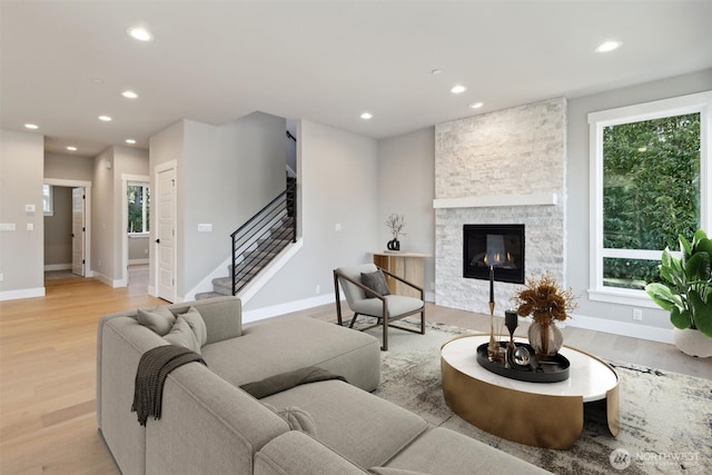 living room with a stone fireplace, stairway, light wood-type flooring, and recessed lighting