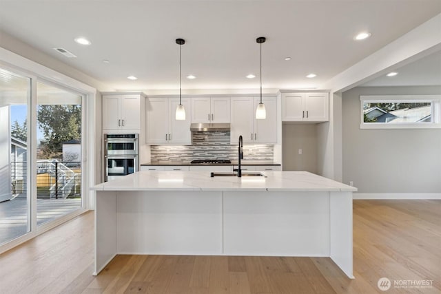 kitchen featuring light wood-style flooring, a sink, visible vents, white cabinets, and decorative backsplash