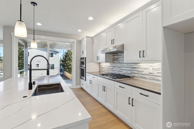 kitchen with stainless steel appliances, white cabinets, a sink, light wood-type flooring, and under cabinet range hood