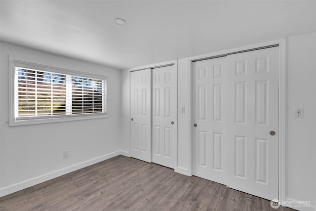 unfurnished bedroom with baseboards, multiple closets, and wood finished floors