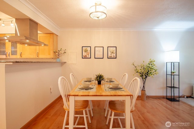 dining area with a textured ceiling, ornamental molding, light wood-style flooring, and baseboards