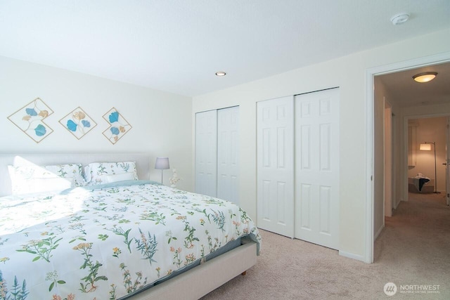 bedroom featuring light carpet, baseboards, and two closets