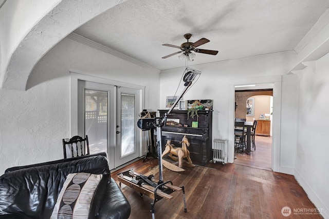 exercise area featuring hardwood / wood-style floors, radiator, a ceiling fan, arched walkways, and ornamental molding