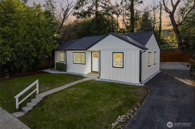 view of front facade with driveway, roof with shingles, board and batten siding, and a yard