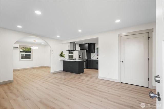 kitchen featuring arched walkways, open floor plan, light countertops, wall chimney exhaust hood, and stainless steel fridge