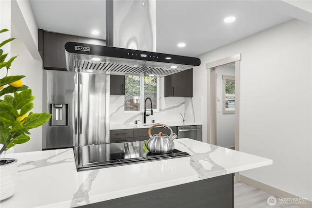 kitchen featuring light stone counters, a sink, appliances with stainless steel finishes, backsplash, and island exhaust hood