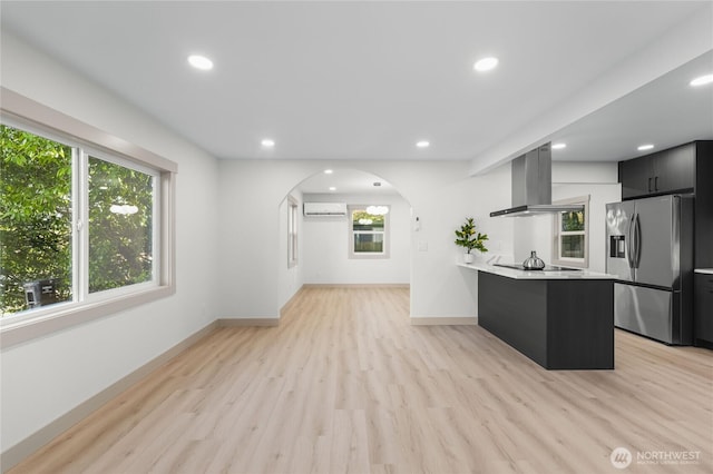 kitchen featuring black electric stovetop, an AC wall unit, light countertops, range hood, and stainless steel fridge