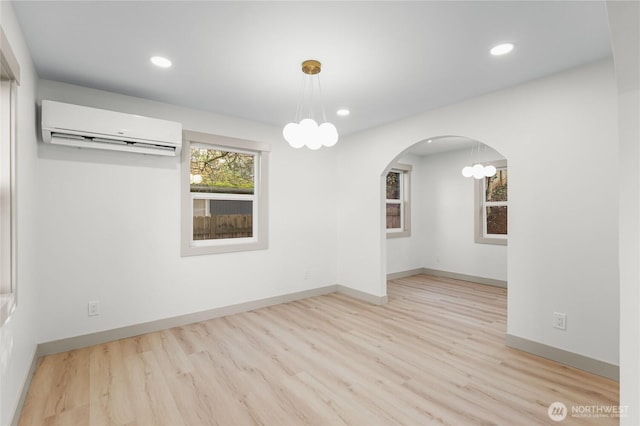 unfurnished room with baseboards, arched walkways, an AC wall unit, and wood finished floors