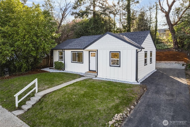 view of front of house featuring board and batten siding, a shingled roof, a front lawn, and fence