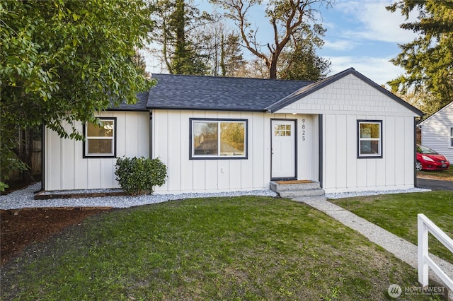 view of front facade with a shingled roof, a front lawn, and board and batten siding