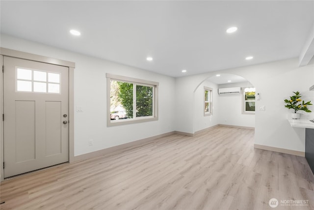 foyer with arched walkways, recessed lighting, baseboards, an AC wall unit, and light wood-type flooring