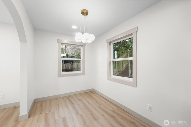 unfurnished room featuring a notable chandelier, baseboards, arched walkways, and wood finished floors