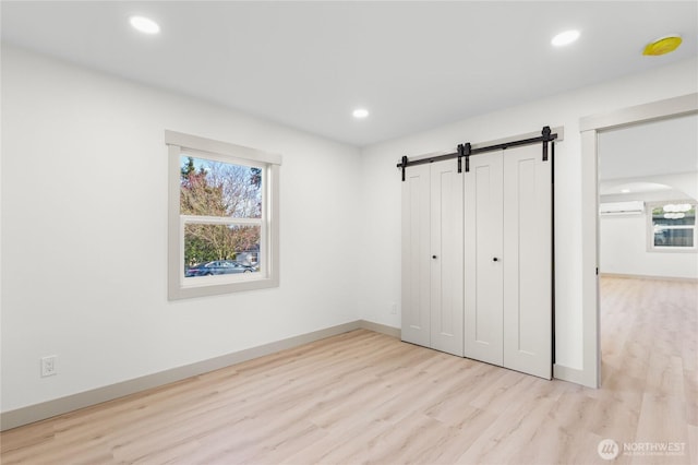 unfurnished bedroom with a barn door, multiple windows, wood finished floors, and recessed lighting