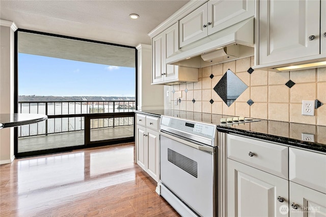 kitchen with light wood-style flooring, under cabinet range hood, white electric range, tasteful backsplash, and white cabinetry