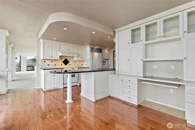 kitchen featuring under cabinet range hood, a peninsula, stainless steel fridge, white cabinetry, and a sink