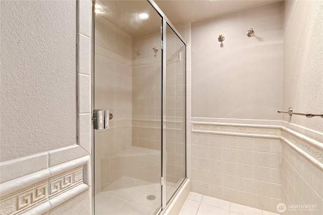 bathroom with tile patterned flooring, a shower stall, tile walls, and a wainscoted wall