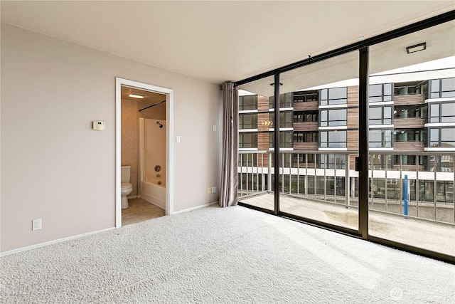 interior space featuring access to exterior, connected bathroom, baseboards, expansive windows, and carpet flooring