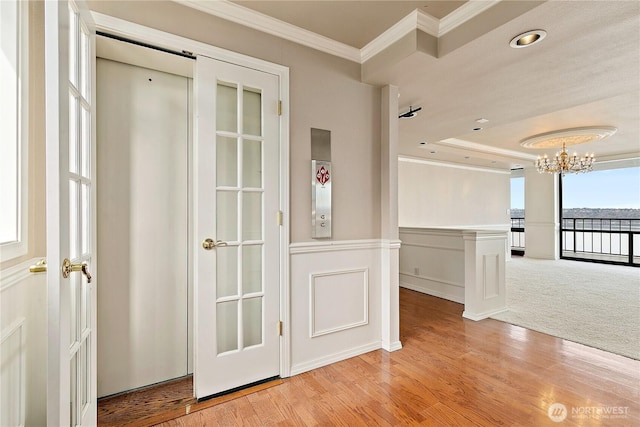 spare room with ornamental molding, wainscoting, light wood-style flooring, a notable chandelier, and a decorative wall