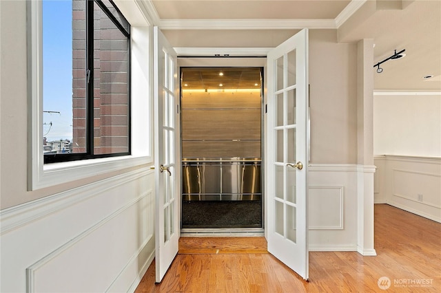 hall featuring a wainscoted wall, light wood-style flooring, ornamental molding, french doors, and a decorative wall