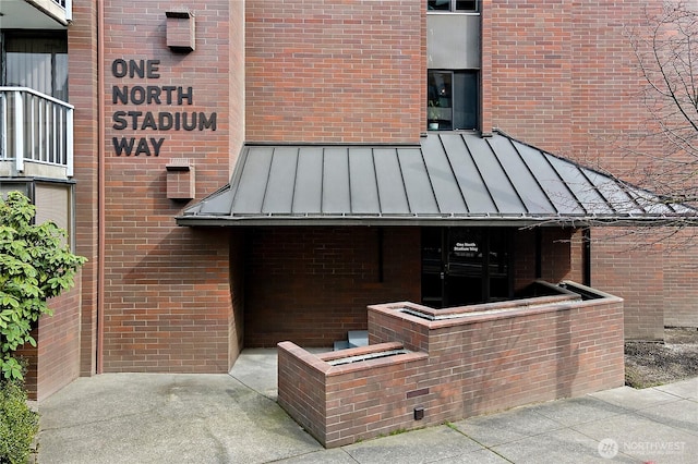 view of exterior entry featuring a standing seam roof, brick siding, and metal roof