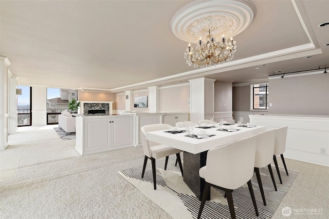 dining room featuring a wainscoted wall, ornamental molding, light carpet, an inviting chandelier, and a raised ceiling