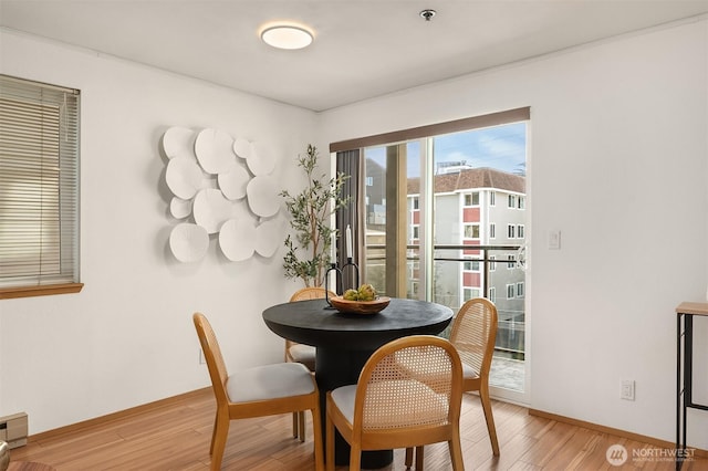 dining space with a baseboard radiator, light wood-style flooring, and baseboards