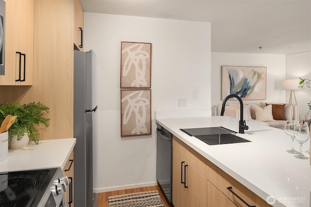 kitchen featuring stainless steel appliances, light brown cabinetry, a sink, and light countertops