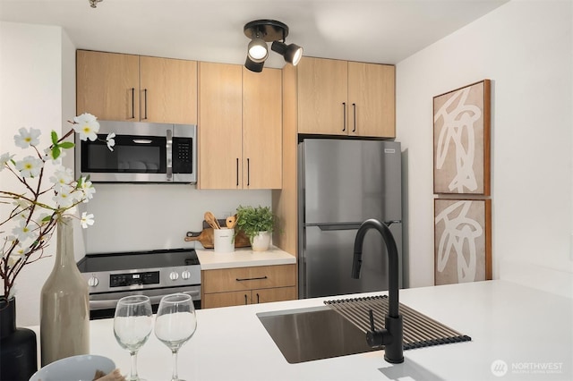 kitchen featuring appliances with stainless steel finishes, light countertops, a sink, and light brown cabinets