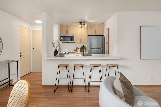 kitchen featuring appliances with stainless steel finishes, a breakfast bar area, light brown cabinets, and light wood-style flooring