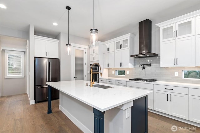 kitchen with dark wood finished floors, backsplash, appliances with stainless steel finishes, a sink, and wall chimney exhaust hood