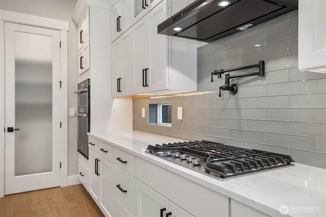 kitchen featuring light stone counters, range hood, stainless steel appliances, white cabinets, and light wood-type flooring