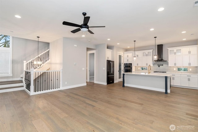 kitchen featuring tasteful backsplash, multiple ovens, light countertops, wall chimney range hood, and high end black refrigerator