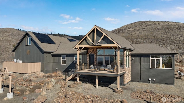 view of front of home featuring a deck with mountain view, roof with shingles, crawl space, board and batten siding, and roof mounted solar panels