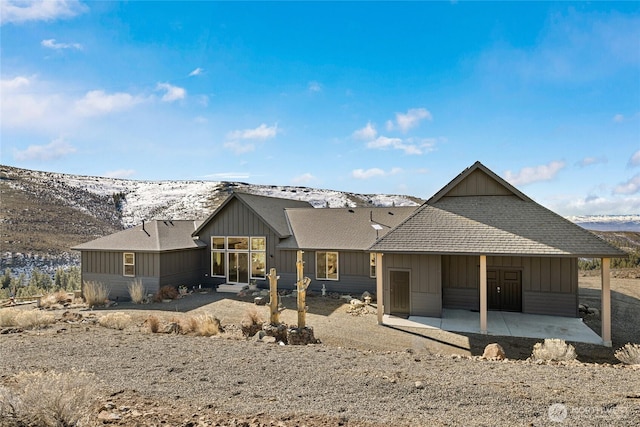 rear view of property with a mountain view, board and batten siding, a shingled roof, and a patio area