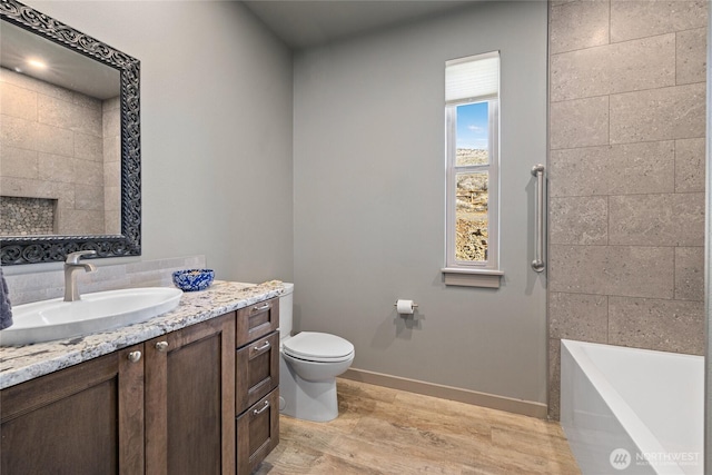 bathroom featuring toilet, wood finished floors, baseboards, a bath, and vanity