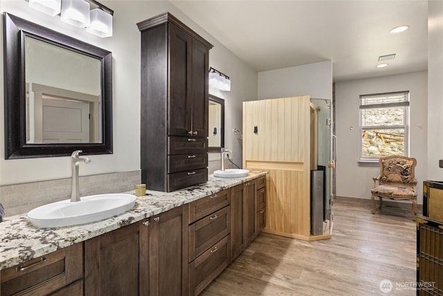 bathroom featuring a sink, a shower with shower door, wood finished floors, and double vanity