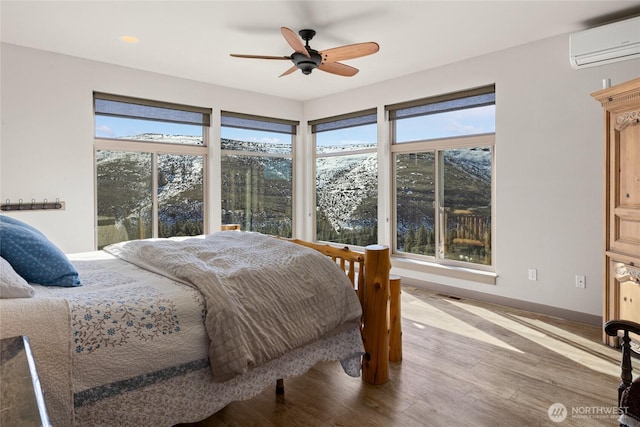 bedroom featuring visible vents, baseboards, wood finished floors, a wall mounted AC, and a ceiling fan