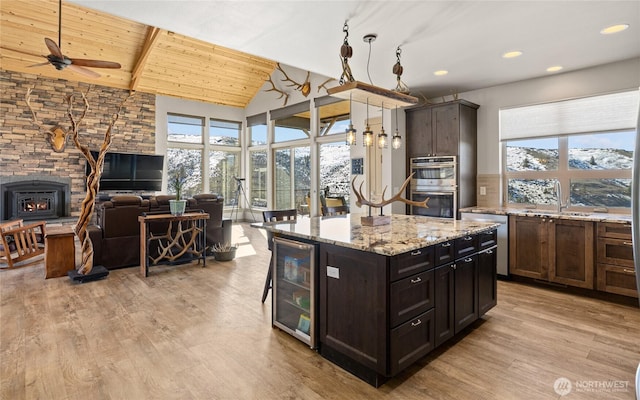 kitchen with a sink, open floor plan, stainless steel appliances, wine cooler, and light wood finished floors