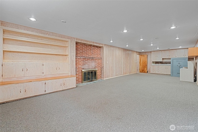 unfurnished living room featuring carpet floors, recessed lighting, a brick fireplace, and wooden walls