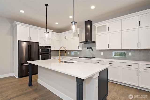 kitchen featuring stainless steel appliances, light countertops, wall chimney range hood, white cabinetry, and a sink