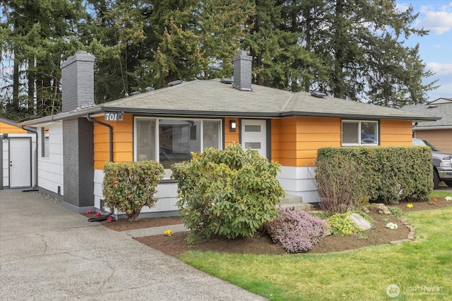 ranch-style home featuring driveway, a shingled roof, and a chimney