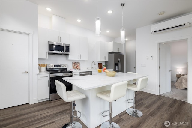 kitchen with a breakfast bar, dark wood-style flooring, a wall unit AC, appliances with stainless steel finishes, and a sink