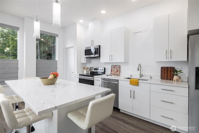 kitchen with light stone counters, a sink, a kitchen breakfast bar, appliances with stainless steel finishes, and pendant lighting