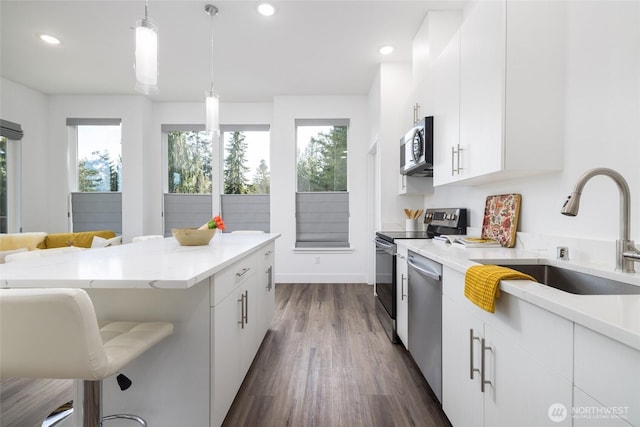 kitchen featuring appliances with stainless steel finishes, a kitchen breakfast bar, dark wood-style flooring, pendant lighting, and a sink