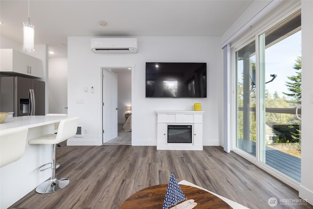 unfurnished living room with dark wood-style flooring, a wall mounted air conditioner, a glass covered fireplace, and baseboards