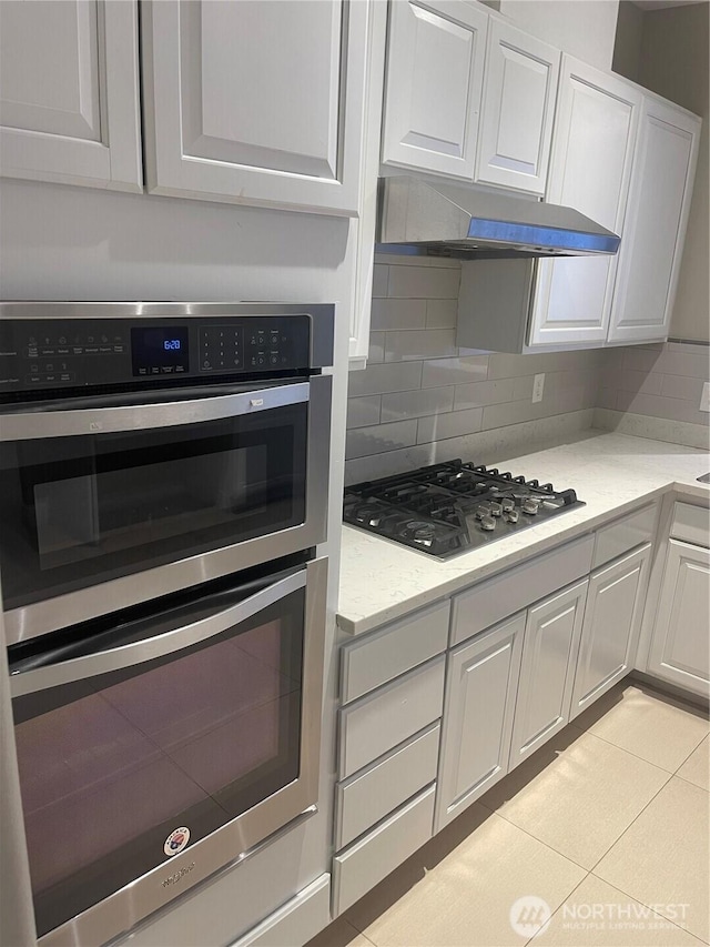 kitchen with under cabinet range hood, tasteful backsplash, white cabinetry, and stainless steel appliances