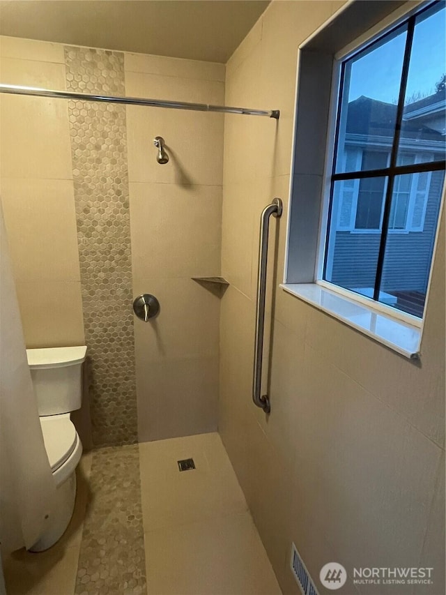 full bathroom with a tile shower and toilet