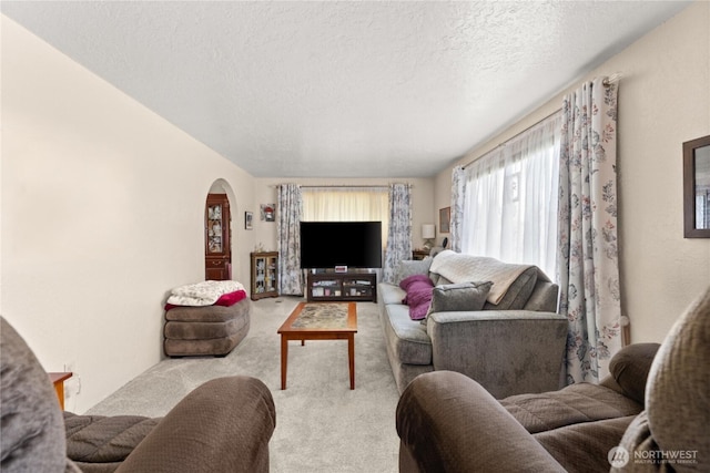 carpeted living room with arched walkways and a textured ceiling
