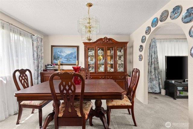 dining space with arched walkways, a textured ceiling, and light colored carpet